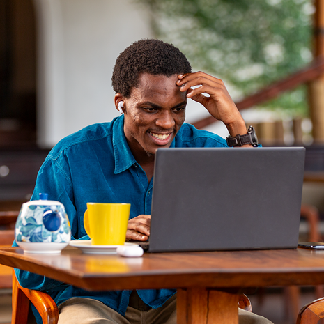 Man in blue shirt looking at laptop and smiling with yellow cup on the table.